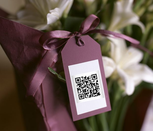 A close-up of a plum-coloured gift tag tied with ribbon to a wrapped bouquet, carrying a qurl code.